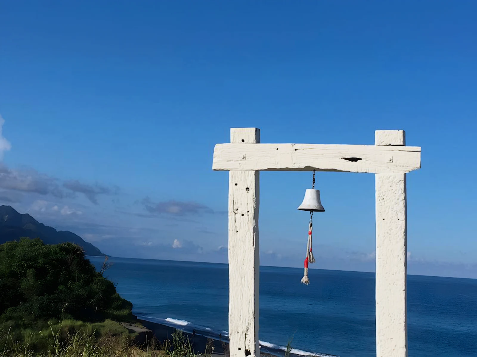 A wooden gate from which a bell is hung overlooks the coast from a bluff above Niushan Beach.