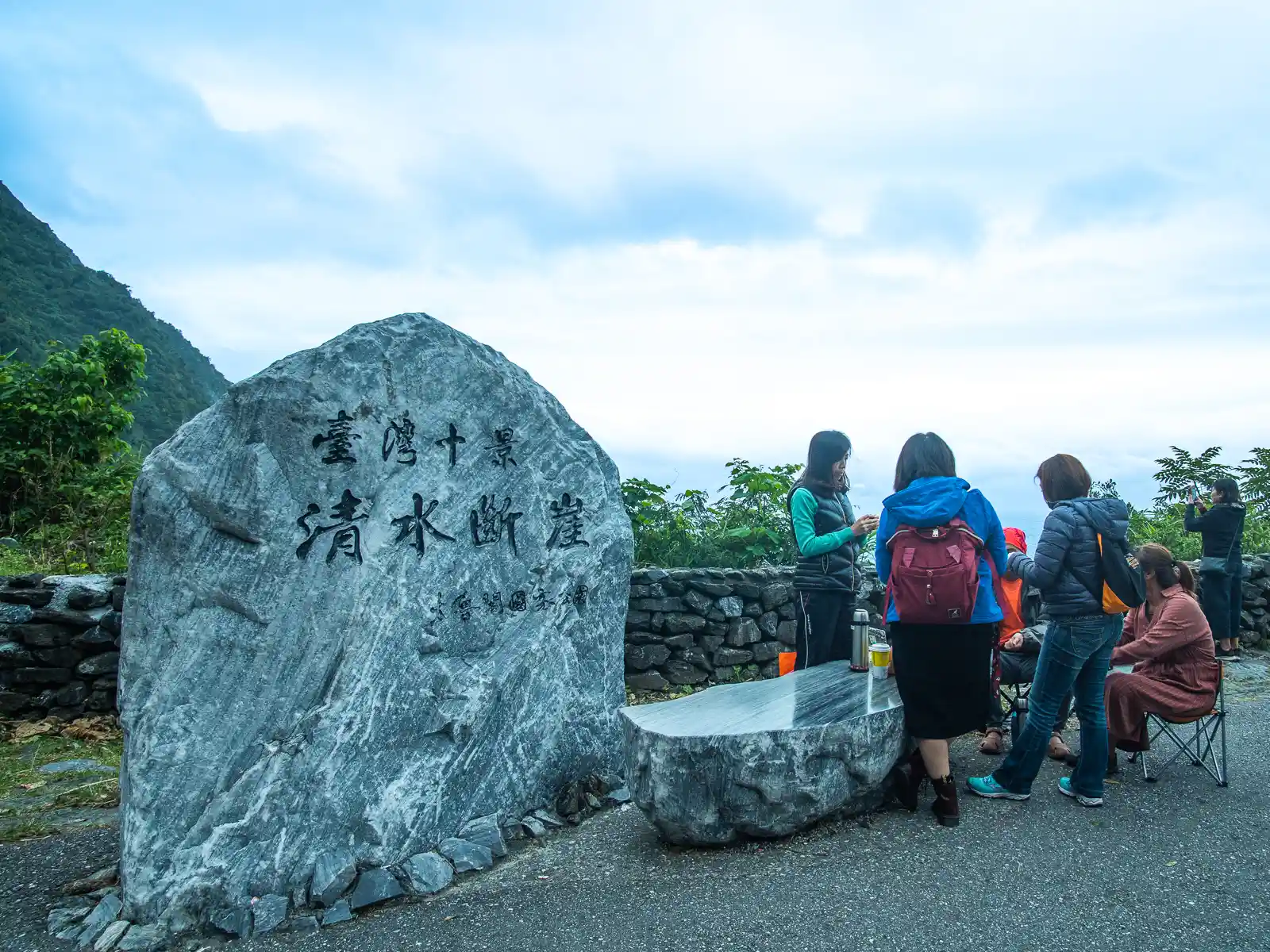 Next to a bench, a large rock is inscribed with the worlds "Qingshui Cliff" in Mandarin.