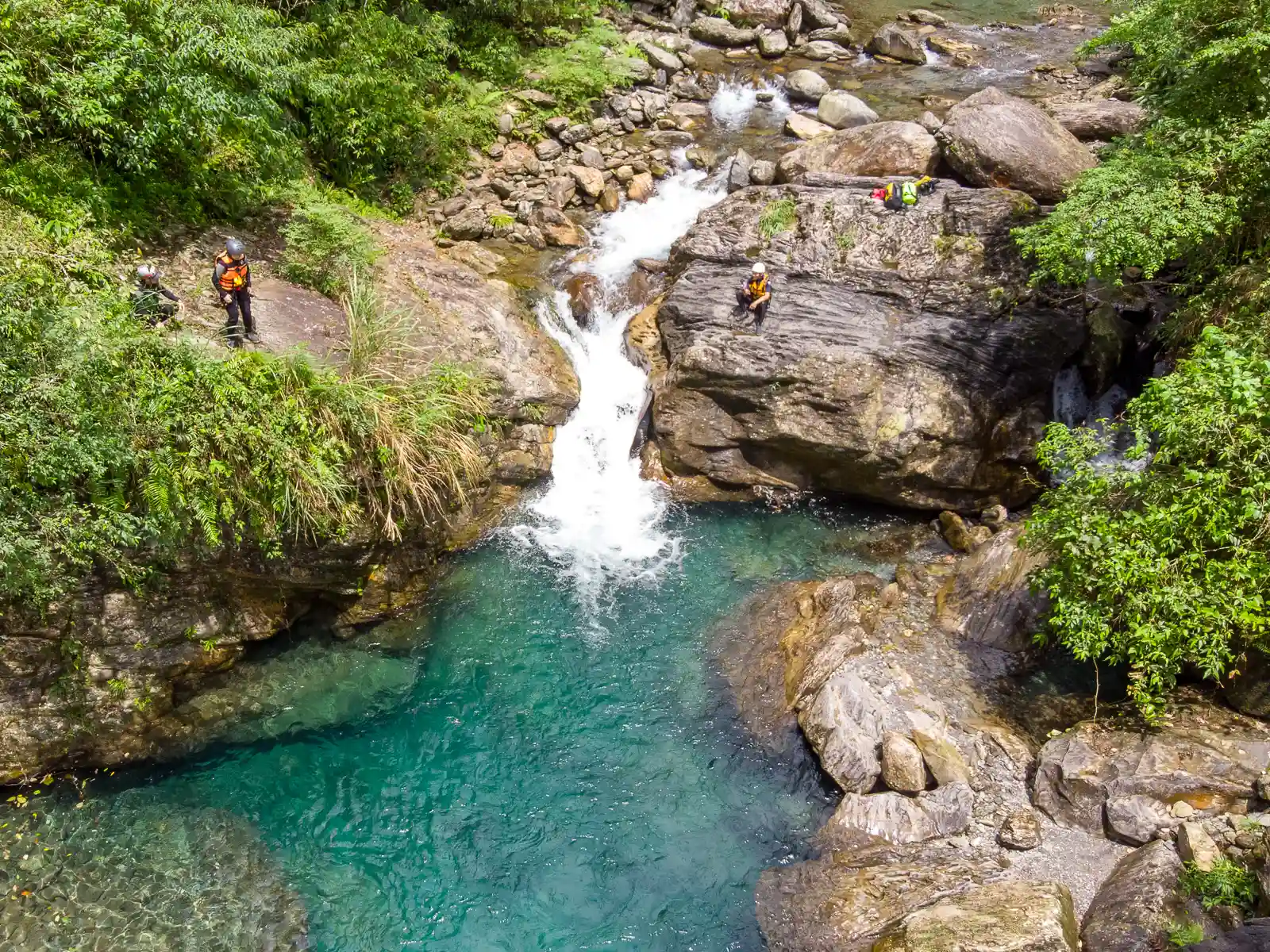 A client is waiting to jump off of a large rock and into a deep pool during a river trace.