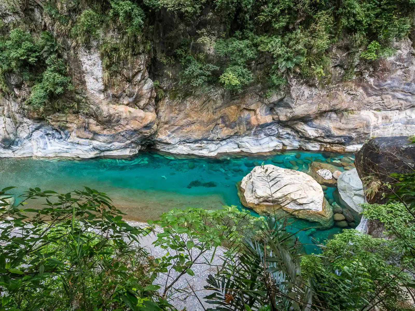 The crystal clear Shakadang River flows through marble canyon surrounded by lush foliage.