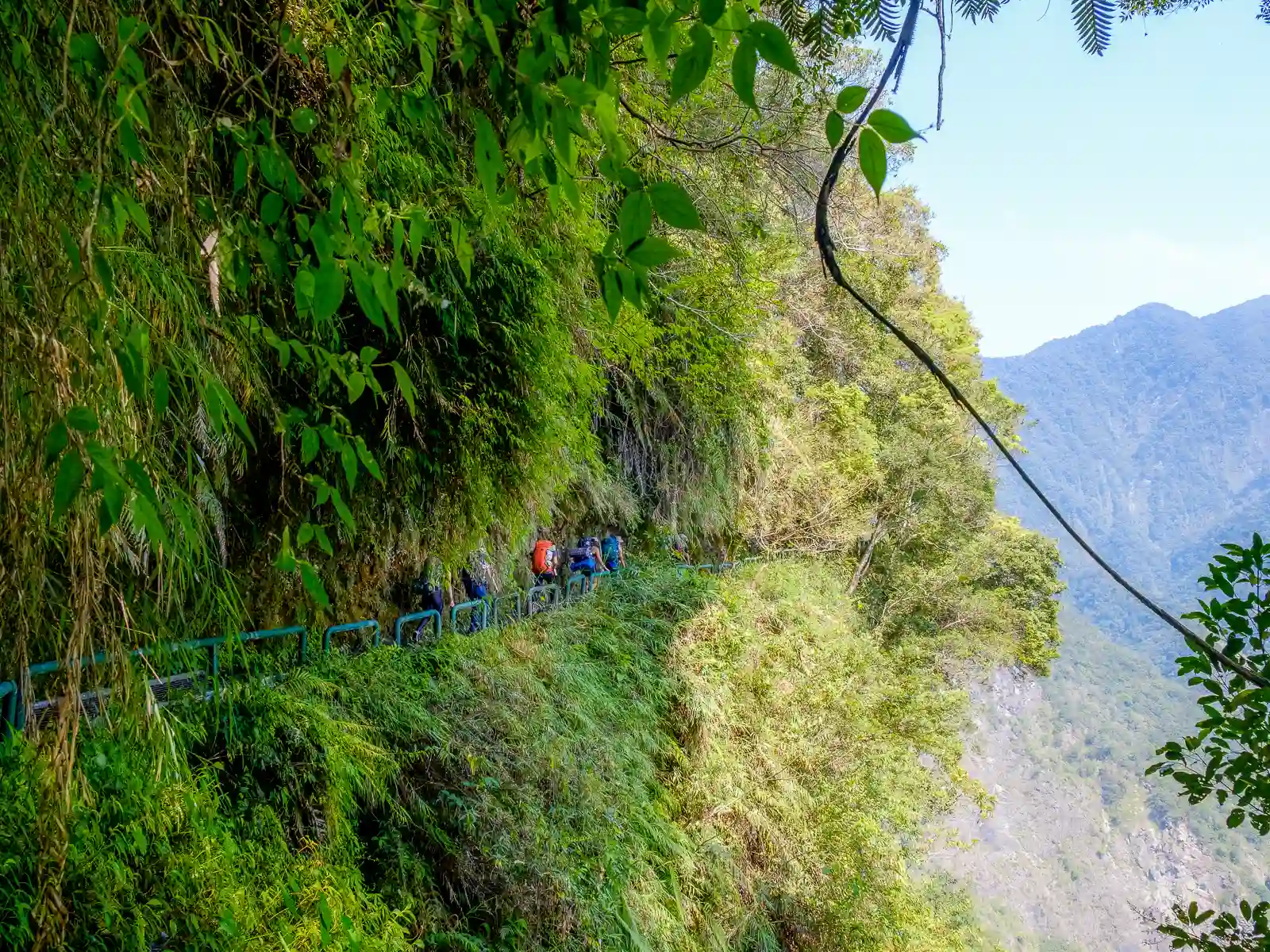 A group of hikers walks along a part of the trail that traverses a cliff face.