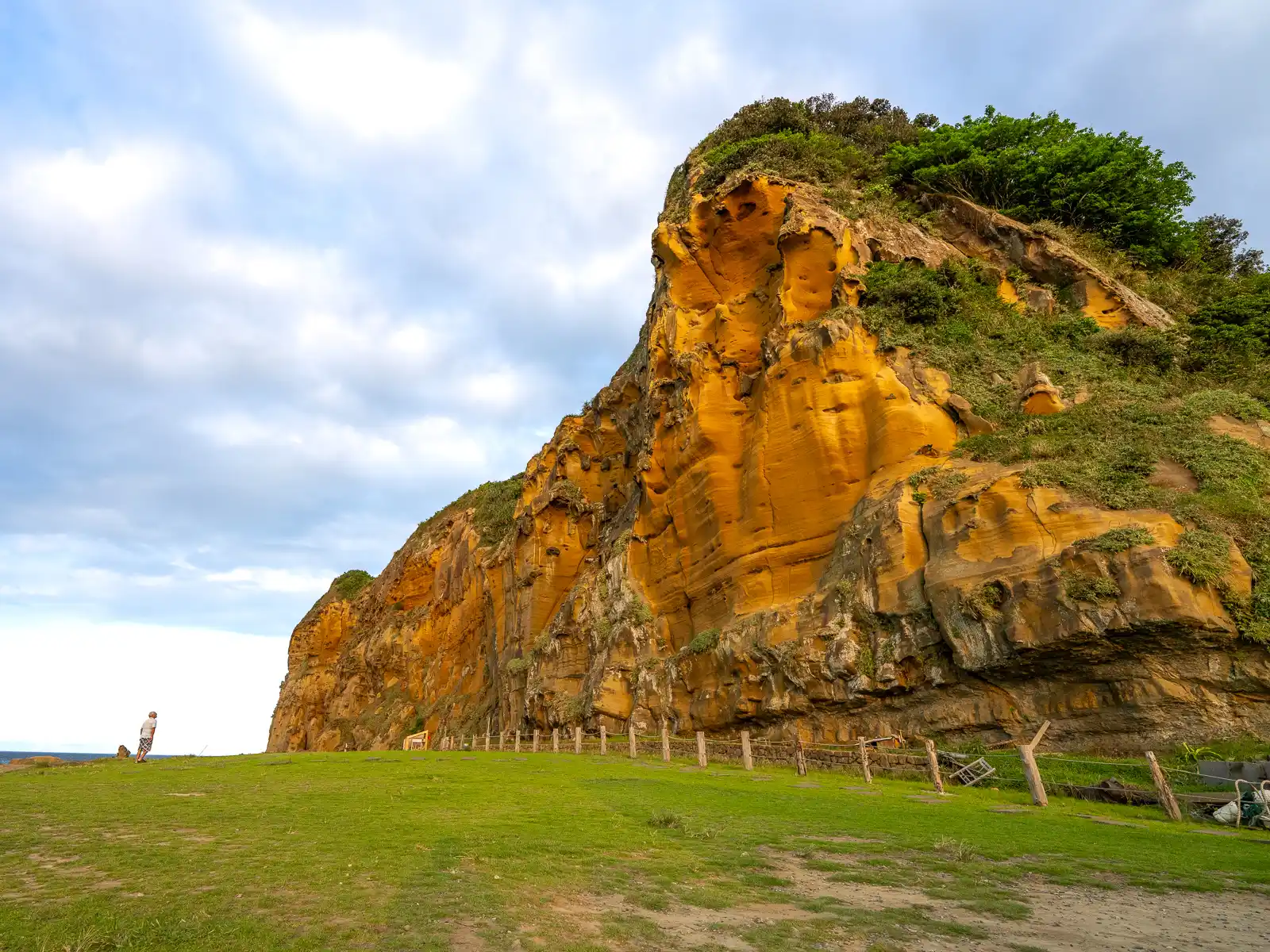 A smooth sandstone cliff rises above the flat grassy area of Fanziao Park.