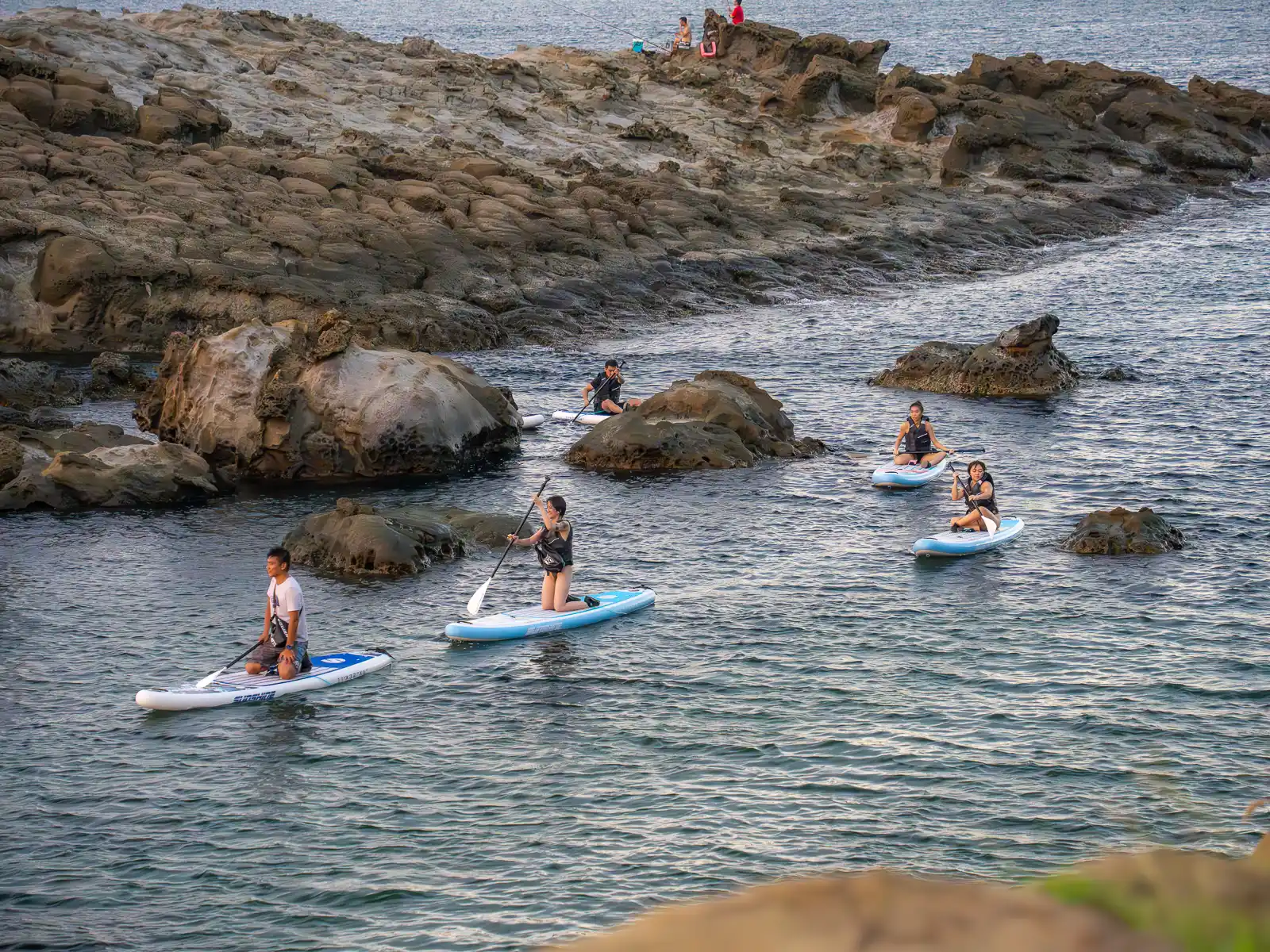 A paddle tour navigates their paddleboards through the shallows next to Fanziao Park.