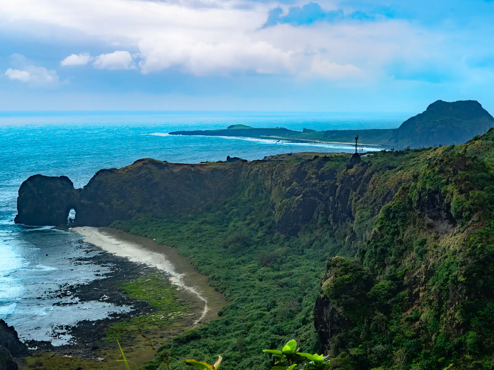 Beneath a rocky promontory, a sandy beach, lush jungle, and volcanic rock all blend together to form a strip of coastline.