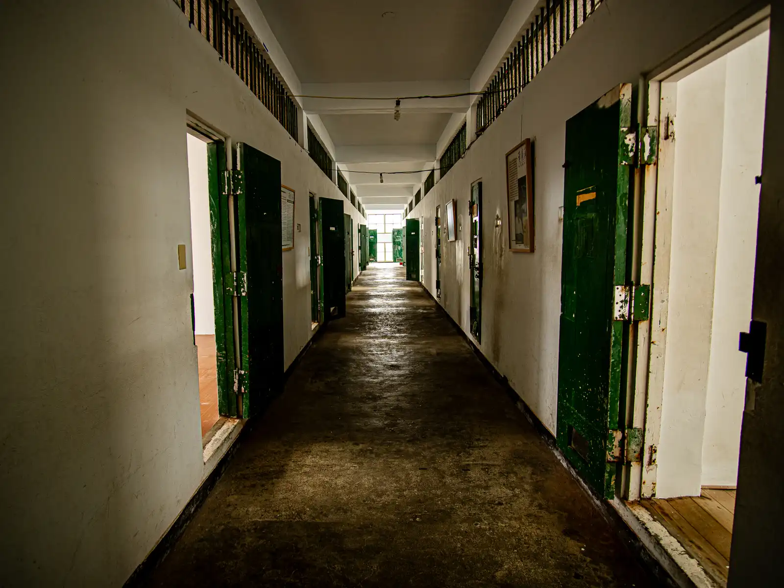A hallway is lined with cells with thick windowless steel doors in either side.
