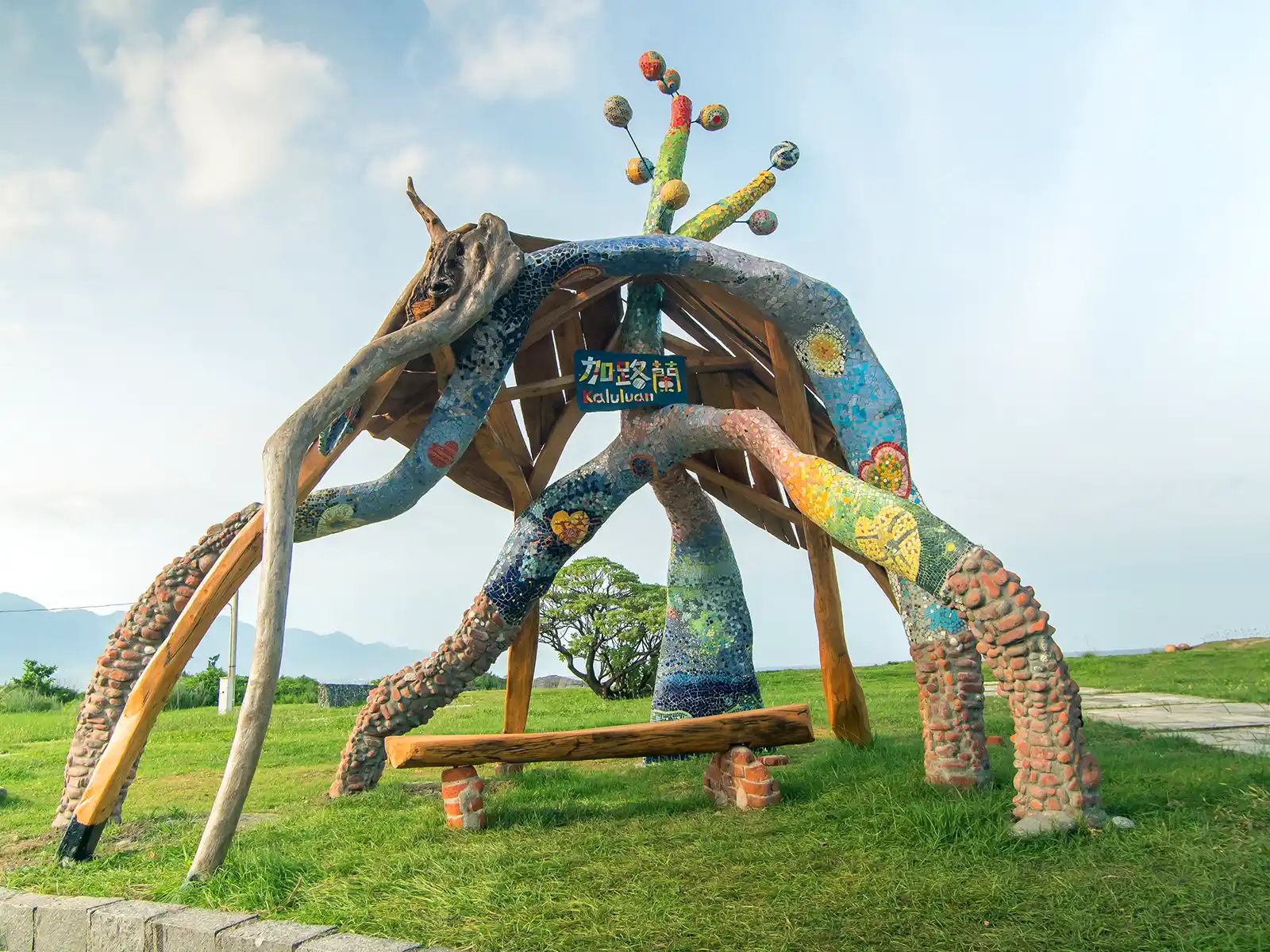 A multi-legged and colorful artwork, that doubles as a shelter covers a bench.