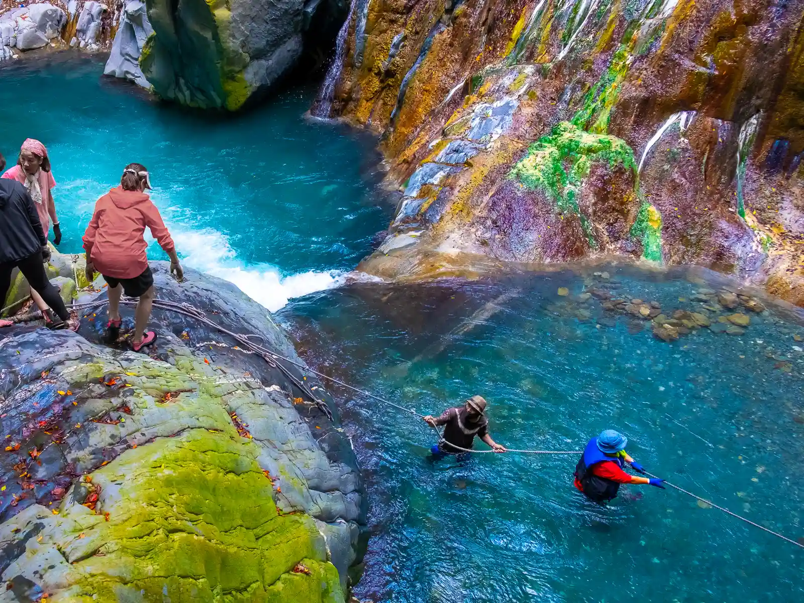 Ropes secure a river crossing in a colorful canyon filled with crystal clear water.