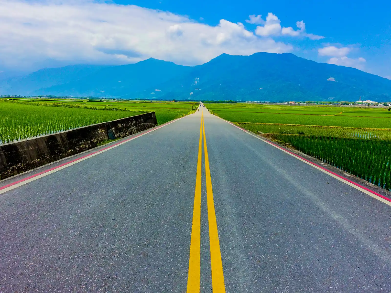 A perfectly straight road leads directly across a valley filled with rice fields.