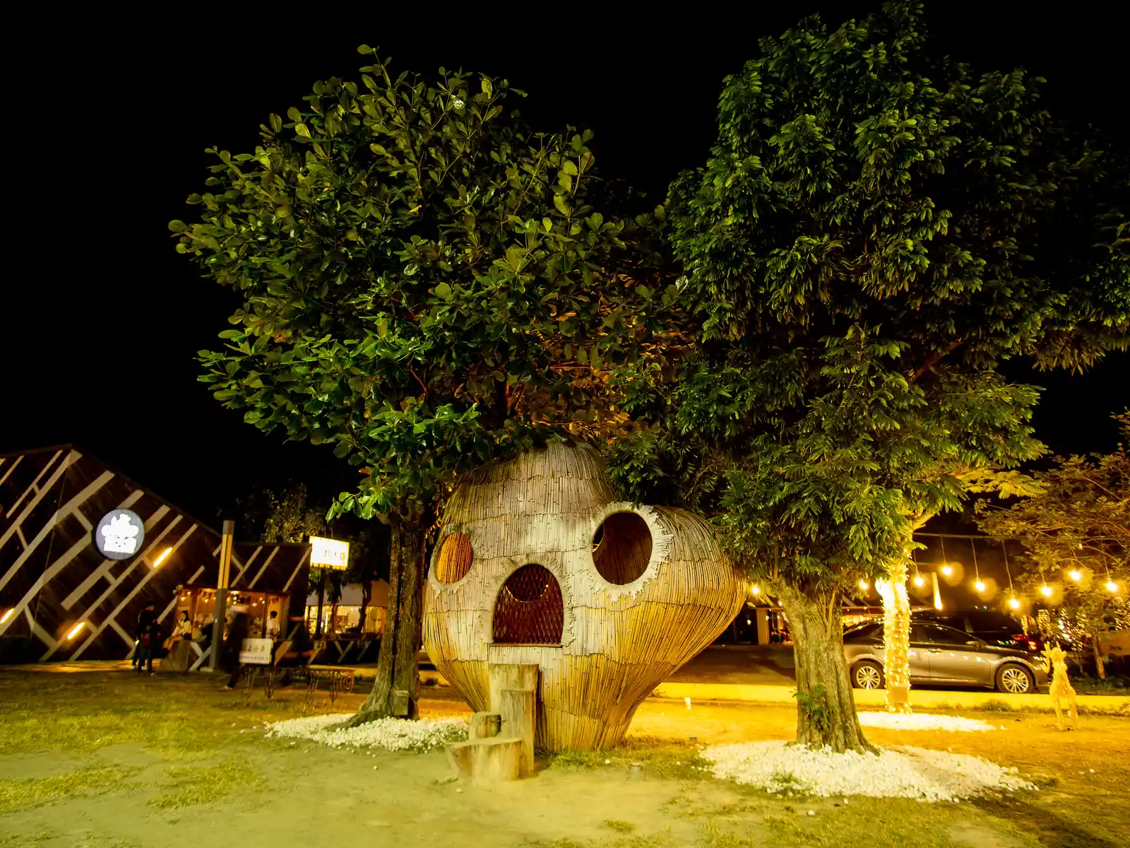 An artistic bamboo hut, shaped like a round face complete with eyes and mouth stands between two trees.