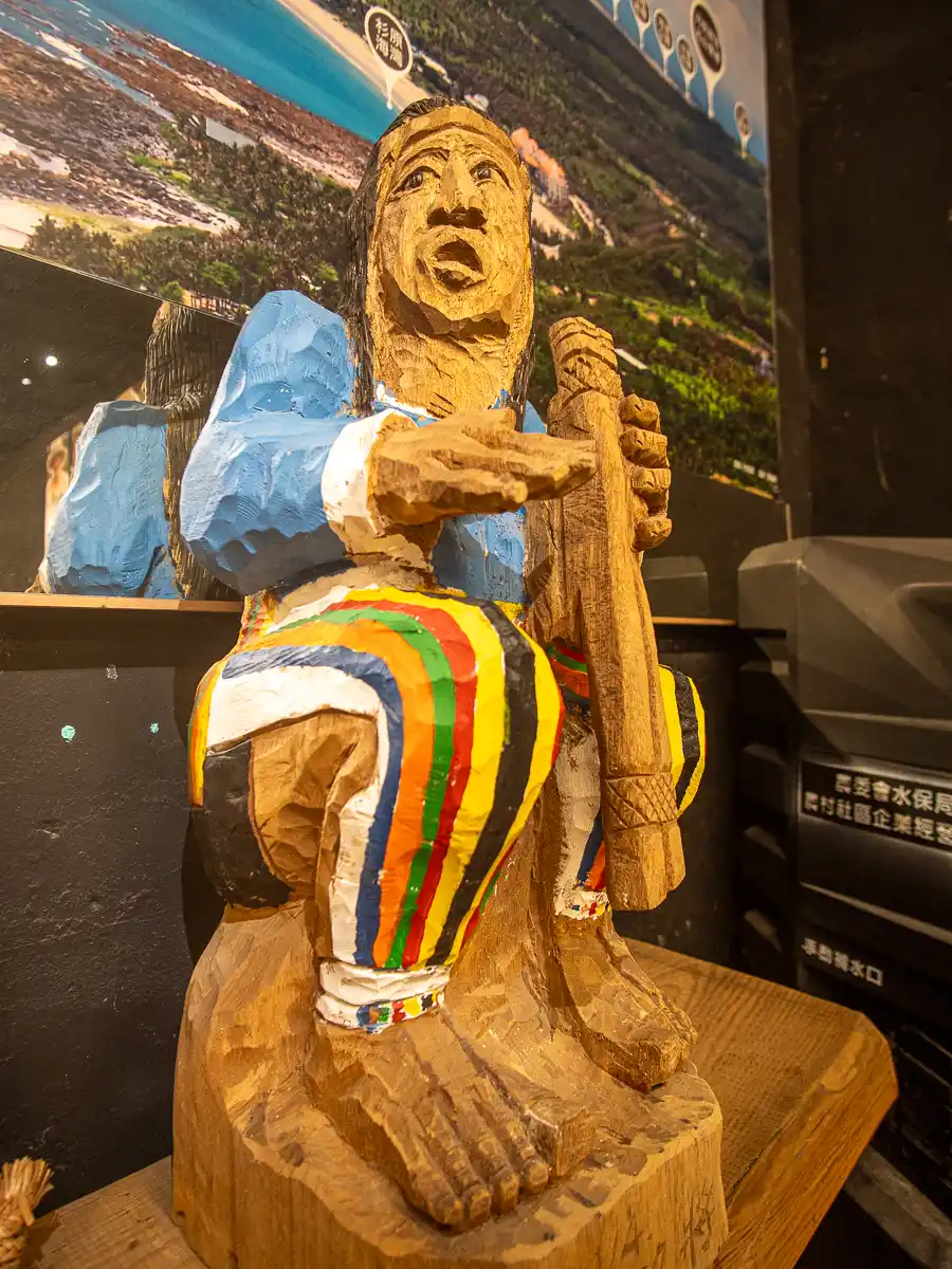 A carved wooden statue depicts and indigenous musician in a traditional outfit.