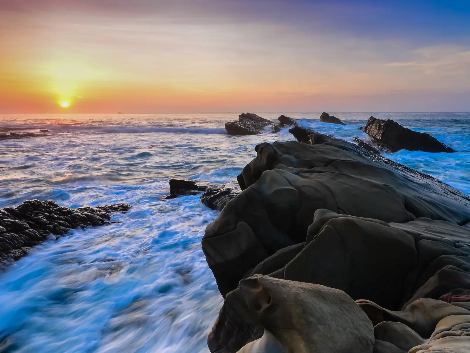 The sun rises as gentle waves crash over the rocks of Xiaoyeliu.