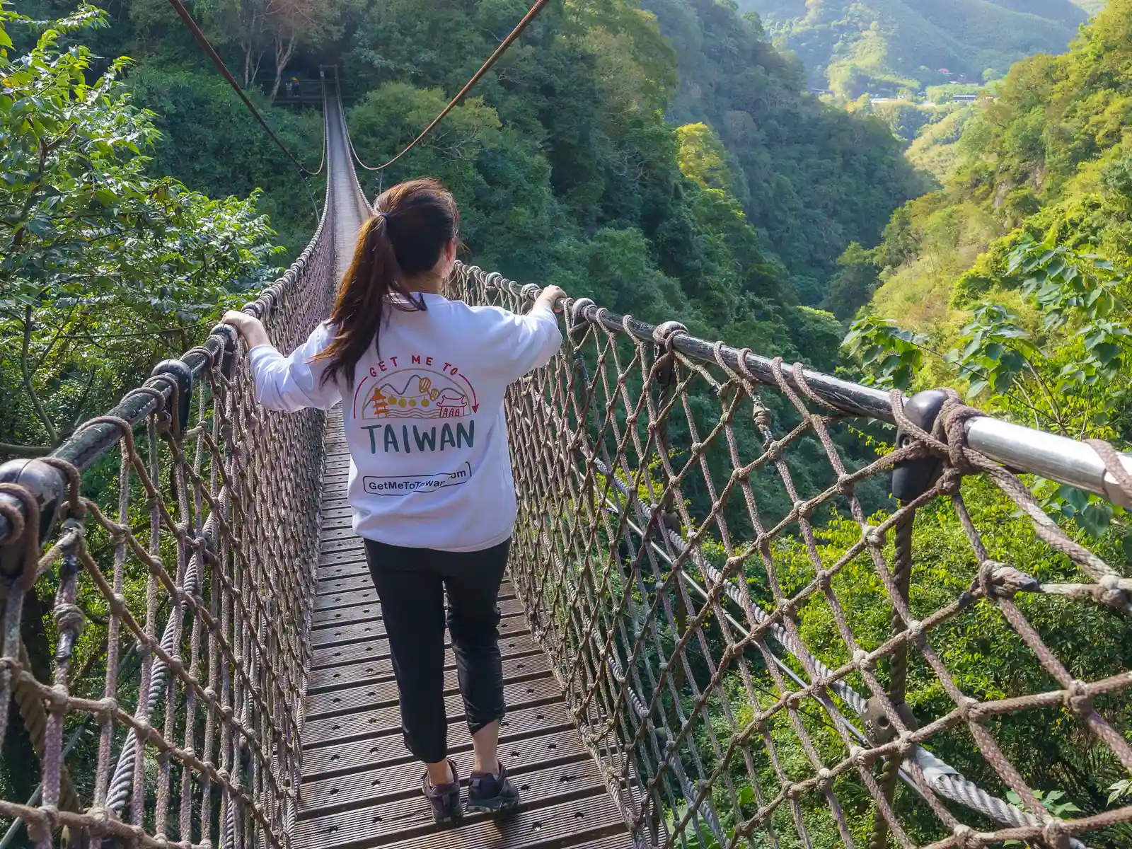 A tourist holds both side of the rope bridge while crossing.
