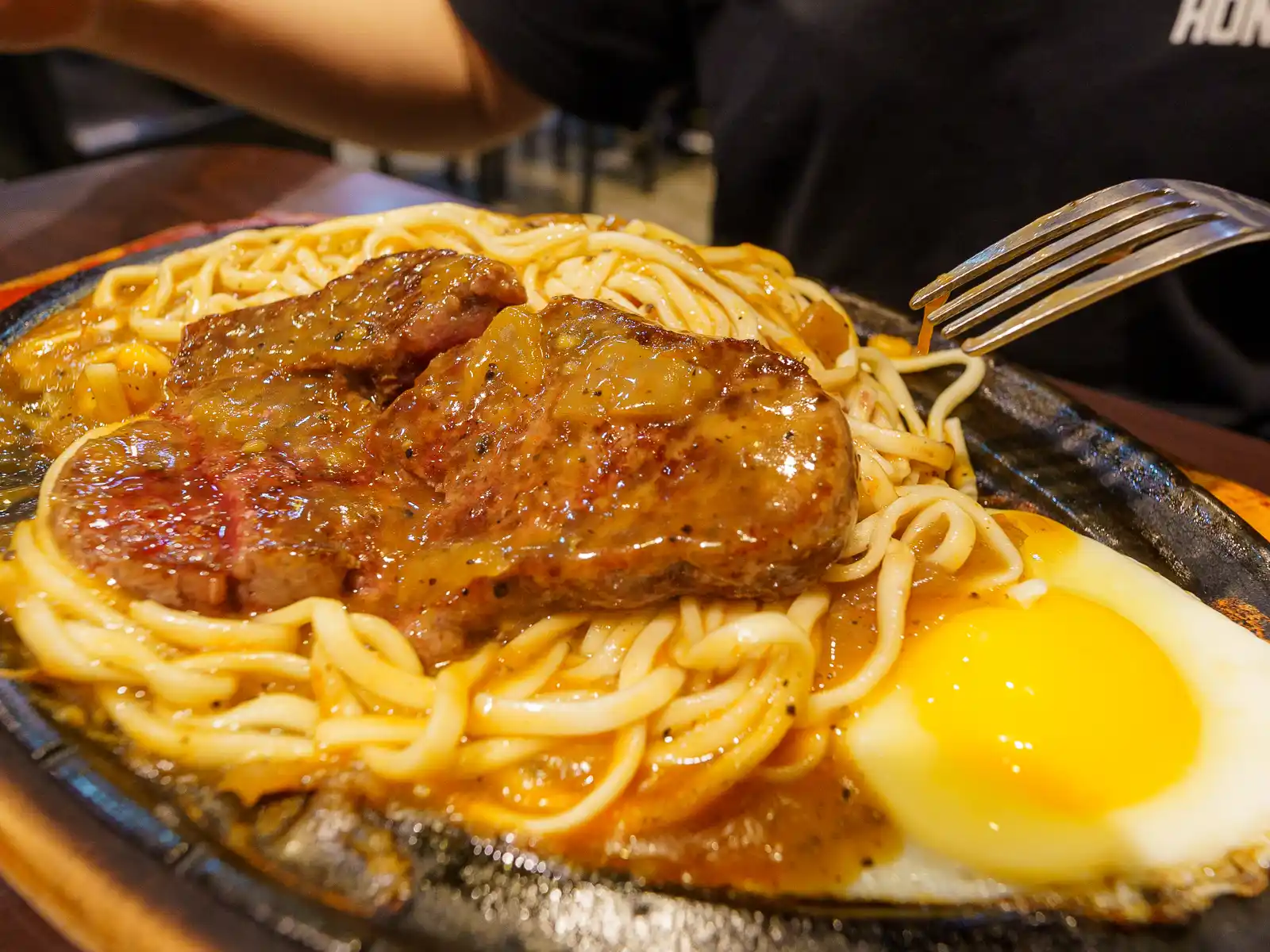 Steak, noodles, and one egg are served on a cast iron plate.