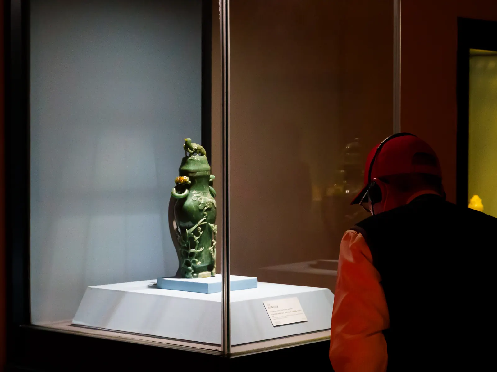A visitor studies an green ornate vase in a glass display.