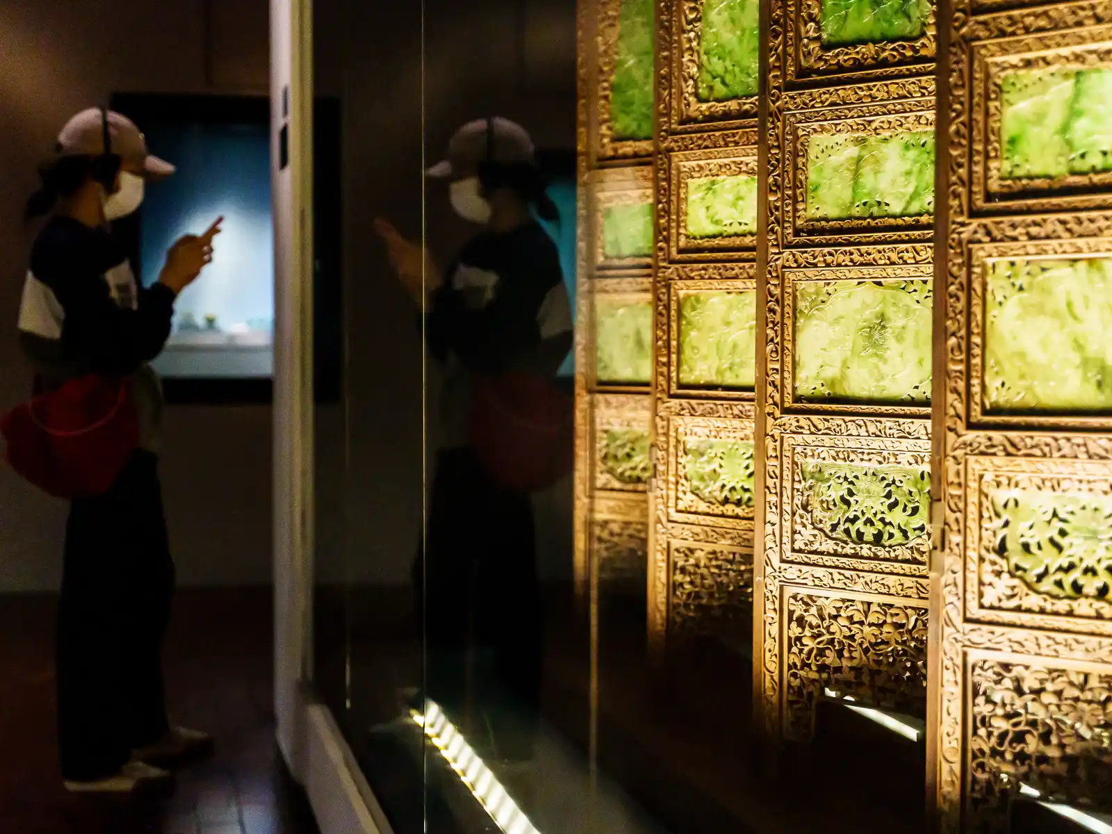 A visitor observing an exhibit of a detailed jade and gold room divider.