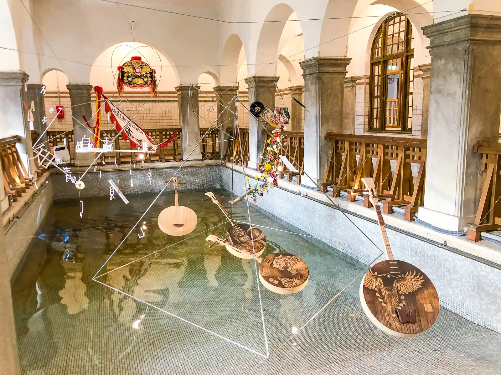 Several Chinese moon guitars are suspended above a bathing pool as part of an exhibition.