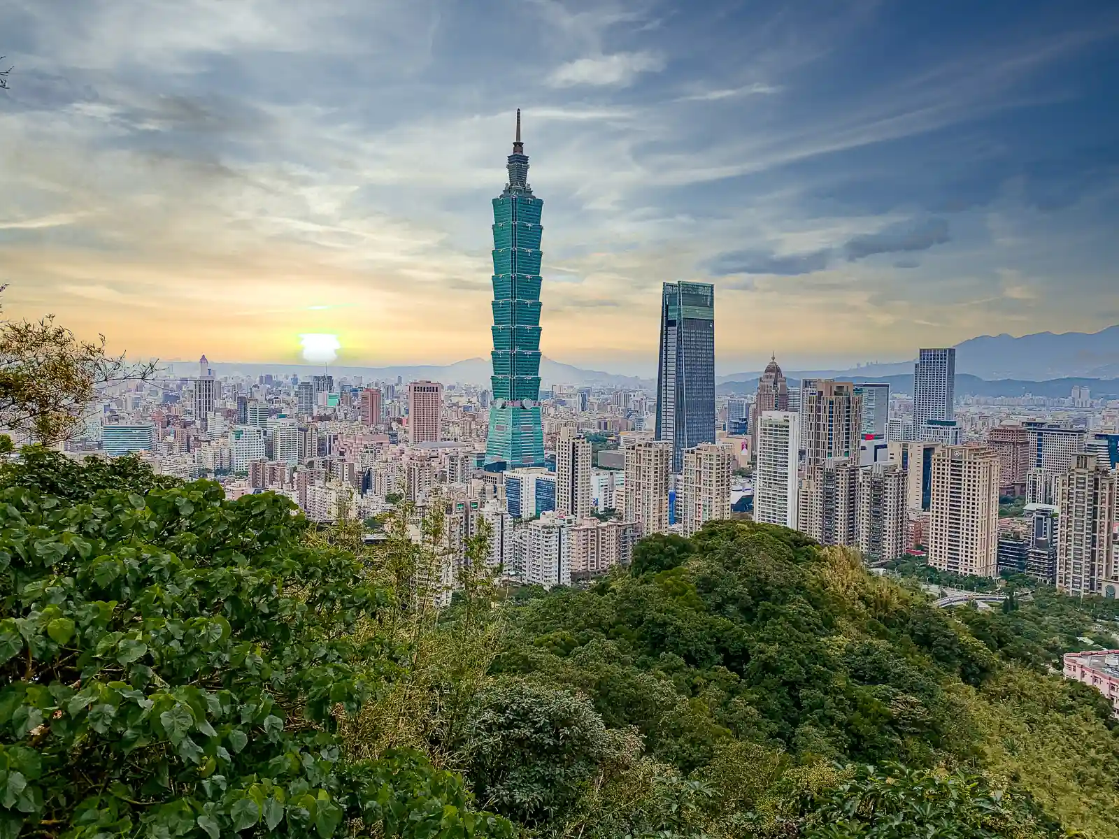 The entirety of the city of Taipei can be seen below and the sun is setting on the horizon.