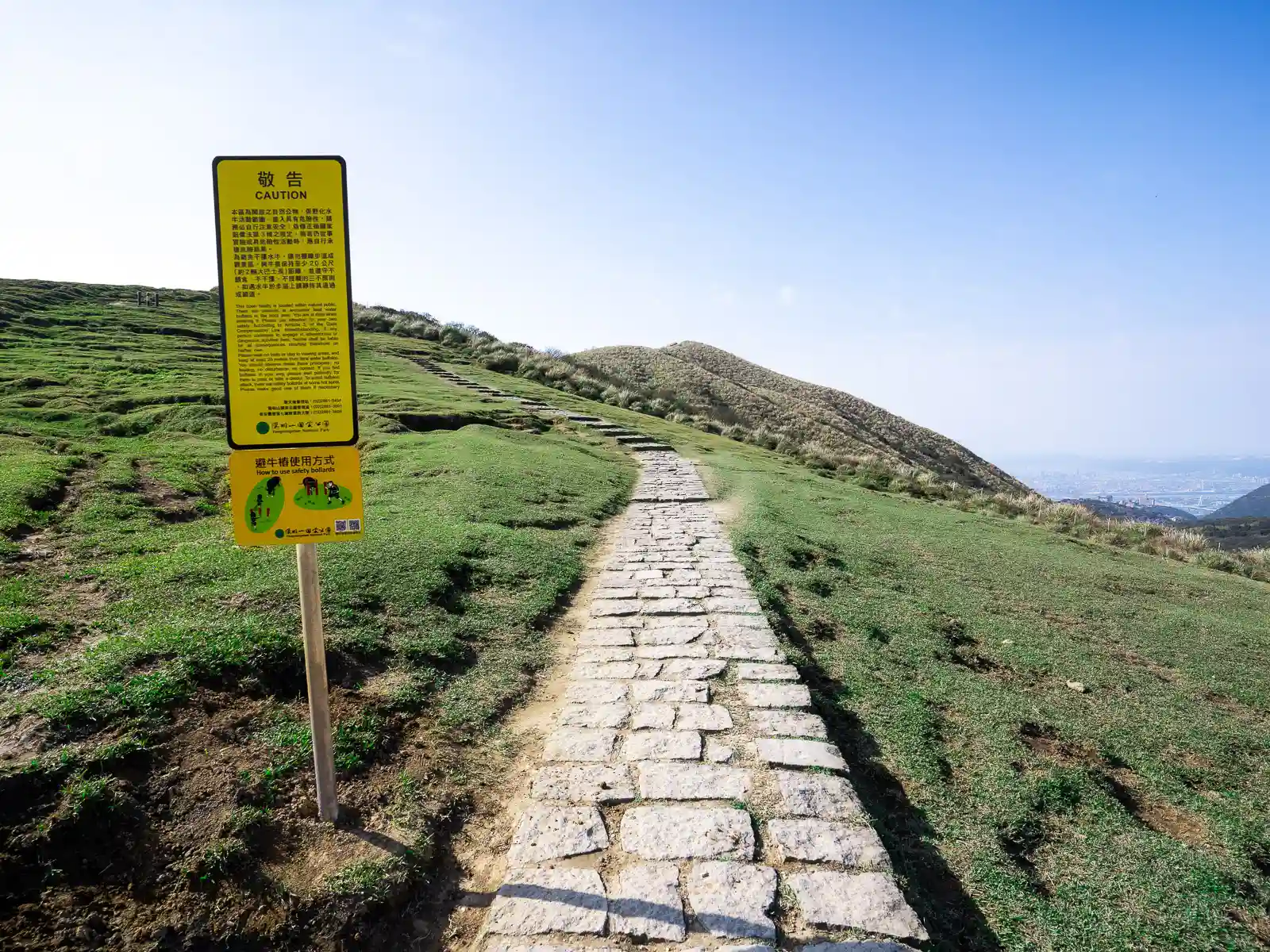 A stone path cuts across a sloping grassland high above Taipei City.