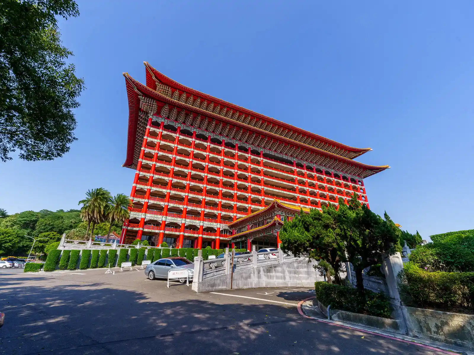 The exterior of a massive red building built in the style of classical Chinese architecture with rows of red columns rising up through each floor.