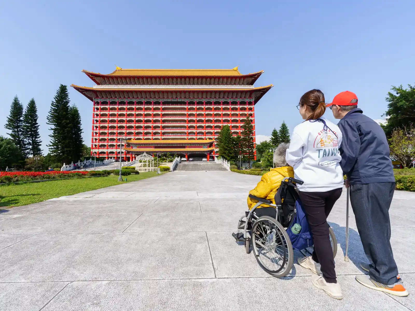 A group of visitors, two of whom are seniors, observe the Grand Hotel from the exterior garden.