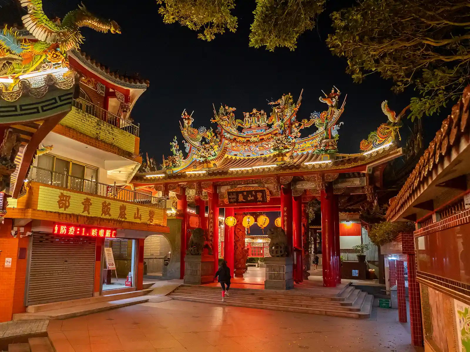 The intricate architecture of a temple courtyard glows at night, illuminated by lanterns and roof lights.