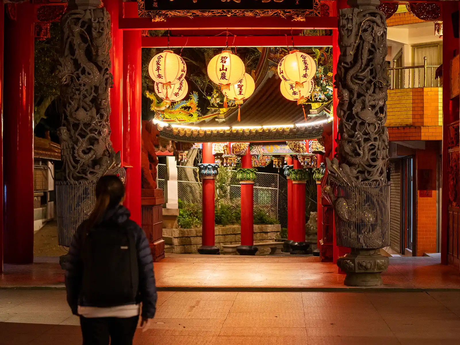 Illuminated Chinese temple entrance at night with red lanterns.