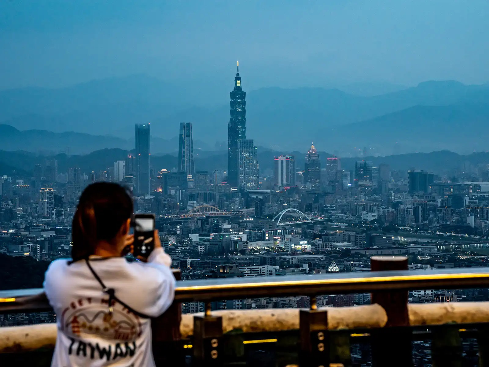 A tourist takes a photo of Taipei 101 and the Taipei Basin at dusk.