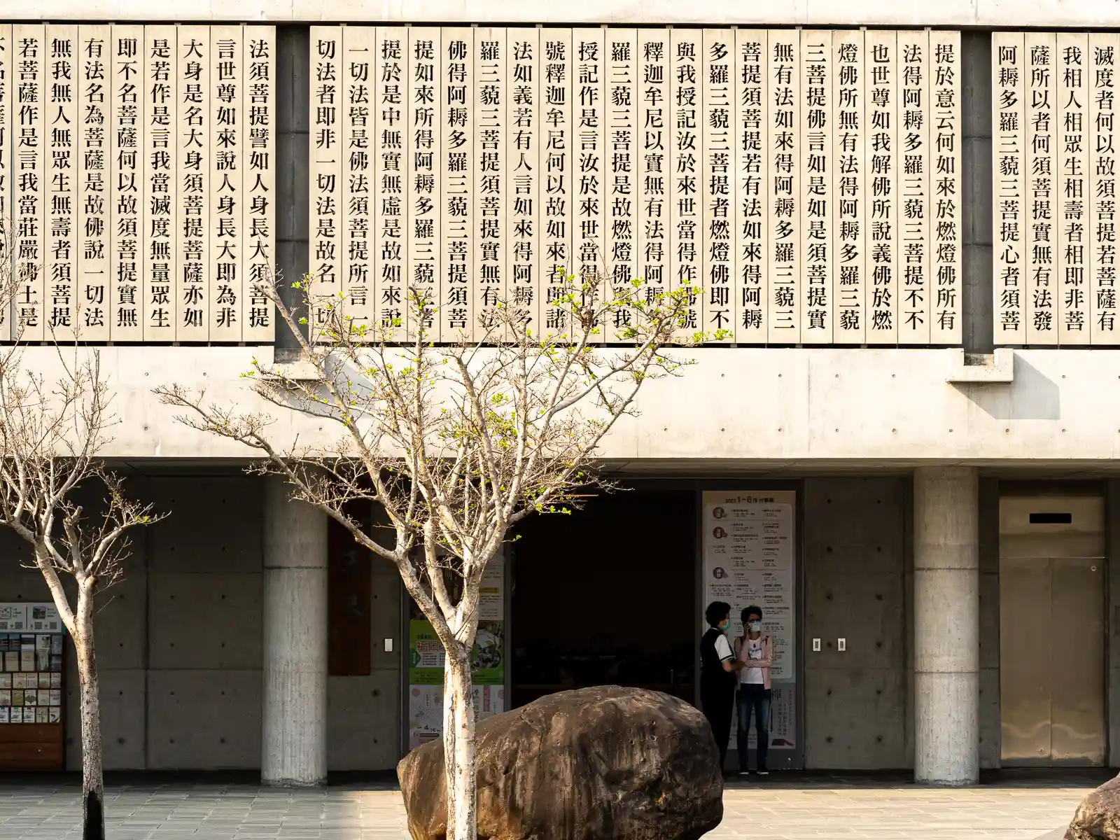 Facade of a building with columns and large text panels in Chinese characters, two people standing by the entrance.