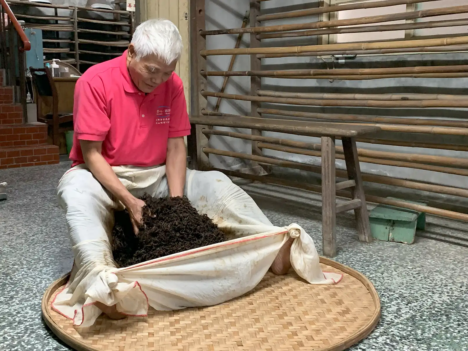 An older man manually tosses tea leaves using a large cloth.