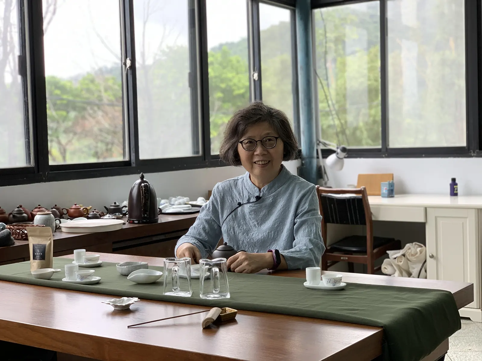 Smiling woman sitting at a tea ceremony table with tea sets.