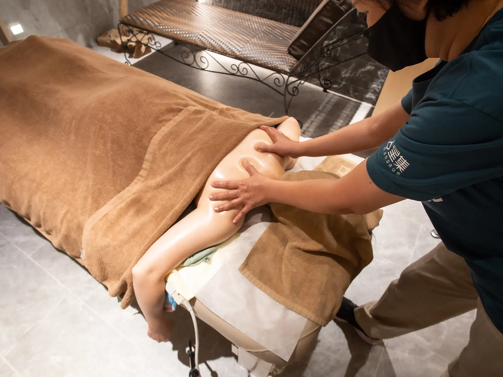 A therapist massaging a client's back covered with a brown towel on a massage bed.