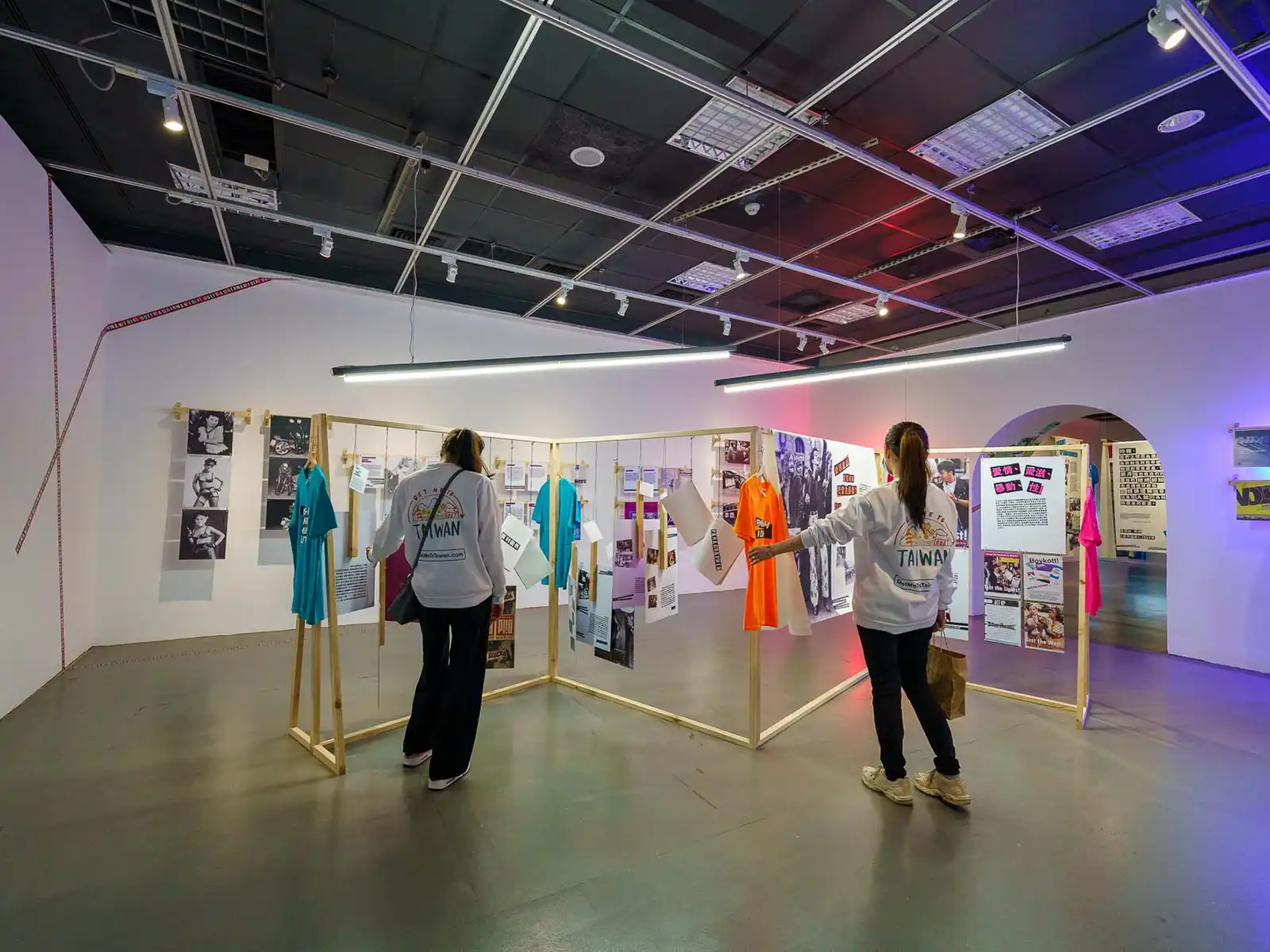 A mixed media exhibition of print media and clothing is mounted on a wooden structure in the middle of the room.