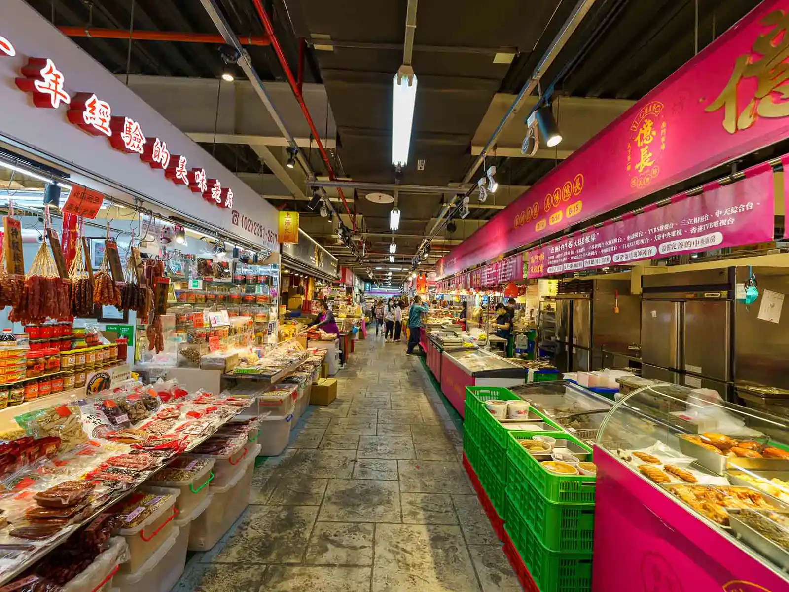 Indoor market aisle with shops selling dried meats and Chinese delicacies, shoppers browsing.