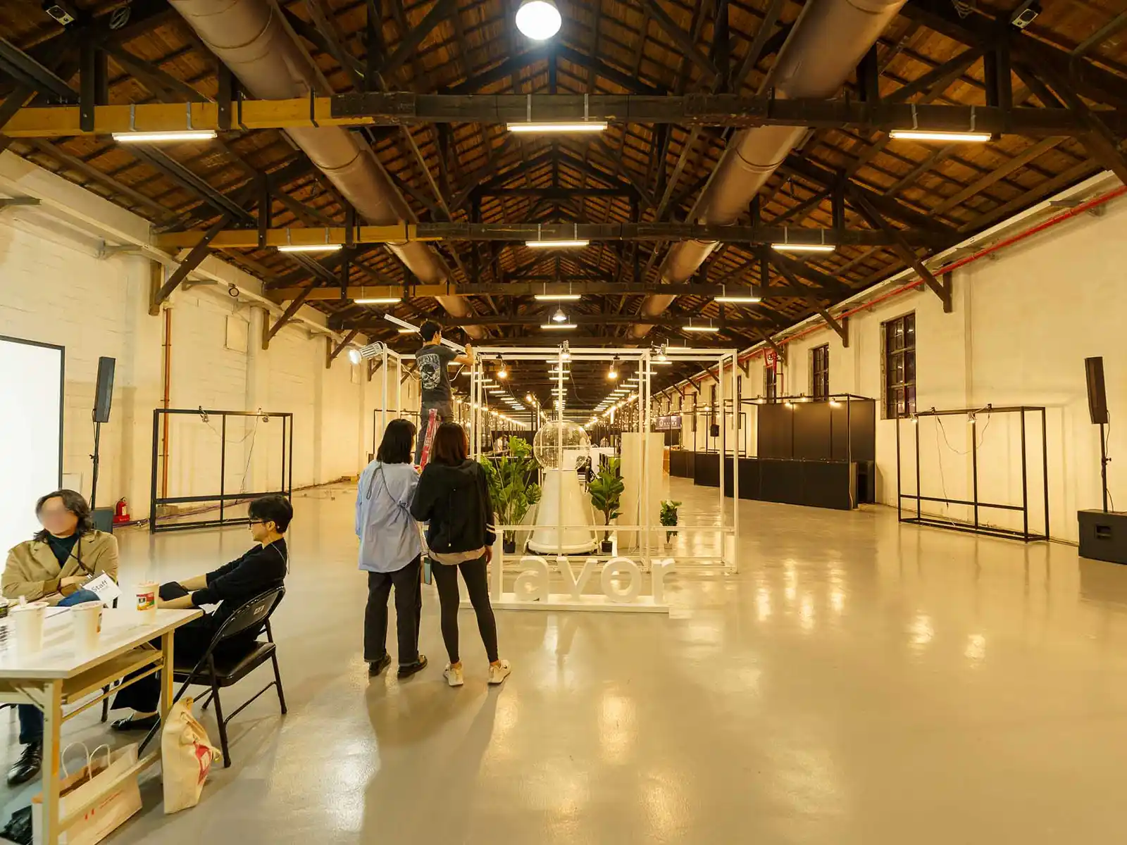 Visitors observing one of many large white and black metal frames that are on display around a warehouse.