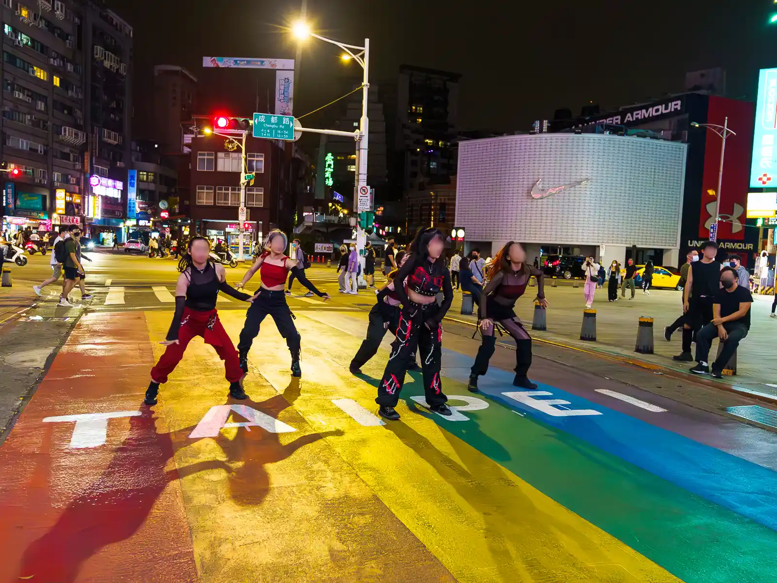 Dancers strike a pose on a rainbow crosswalk at night.