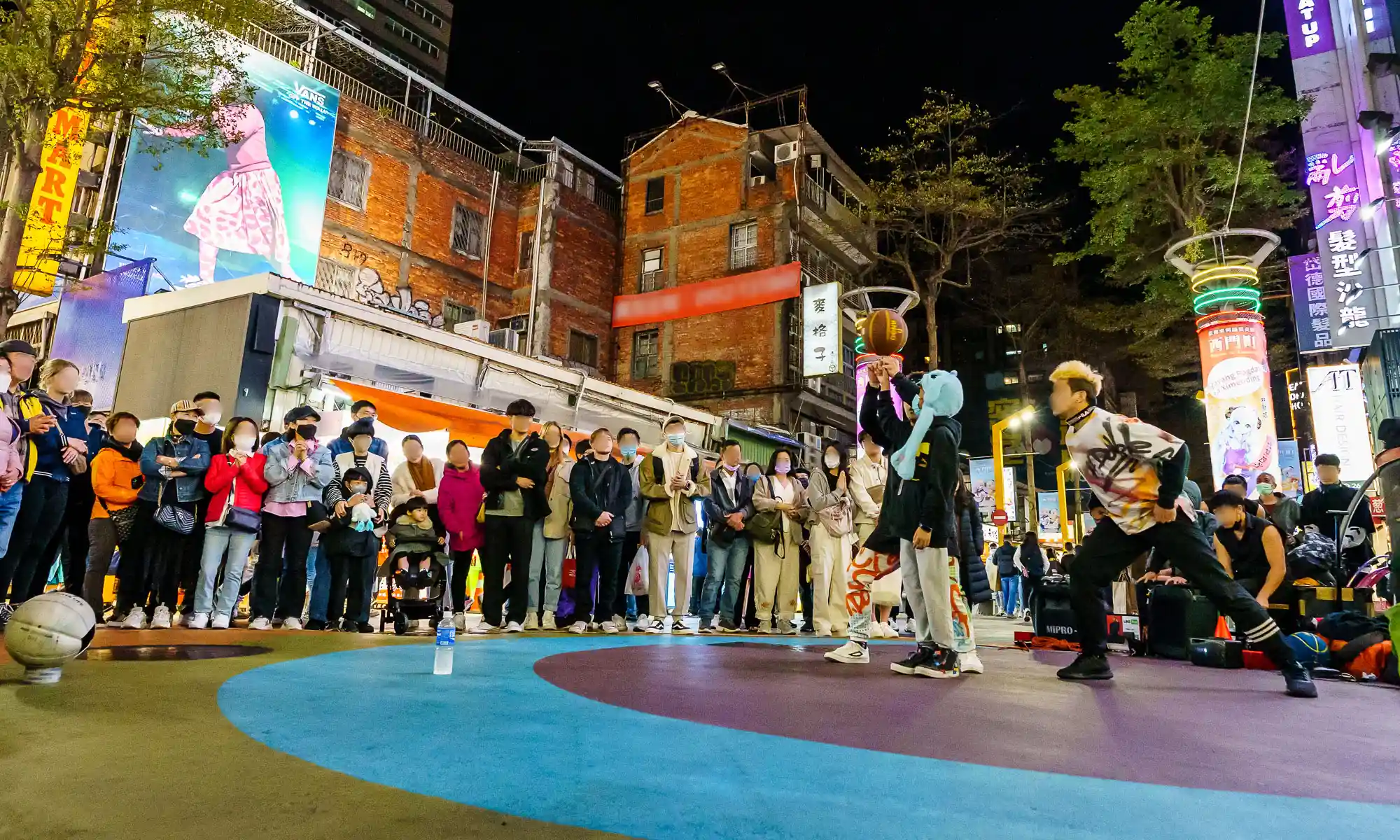 Street performers dancing with a basketball in front of the audience at night.