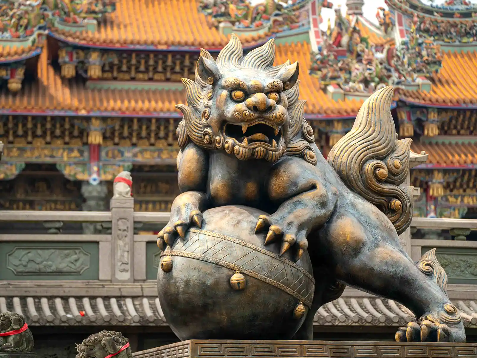 A bronze statue of a lion grasping onto a large ball with the temple in the background.