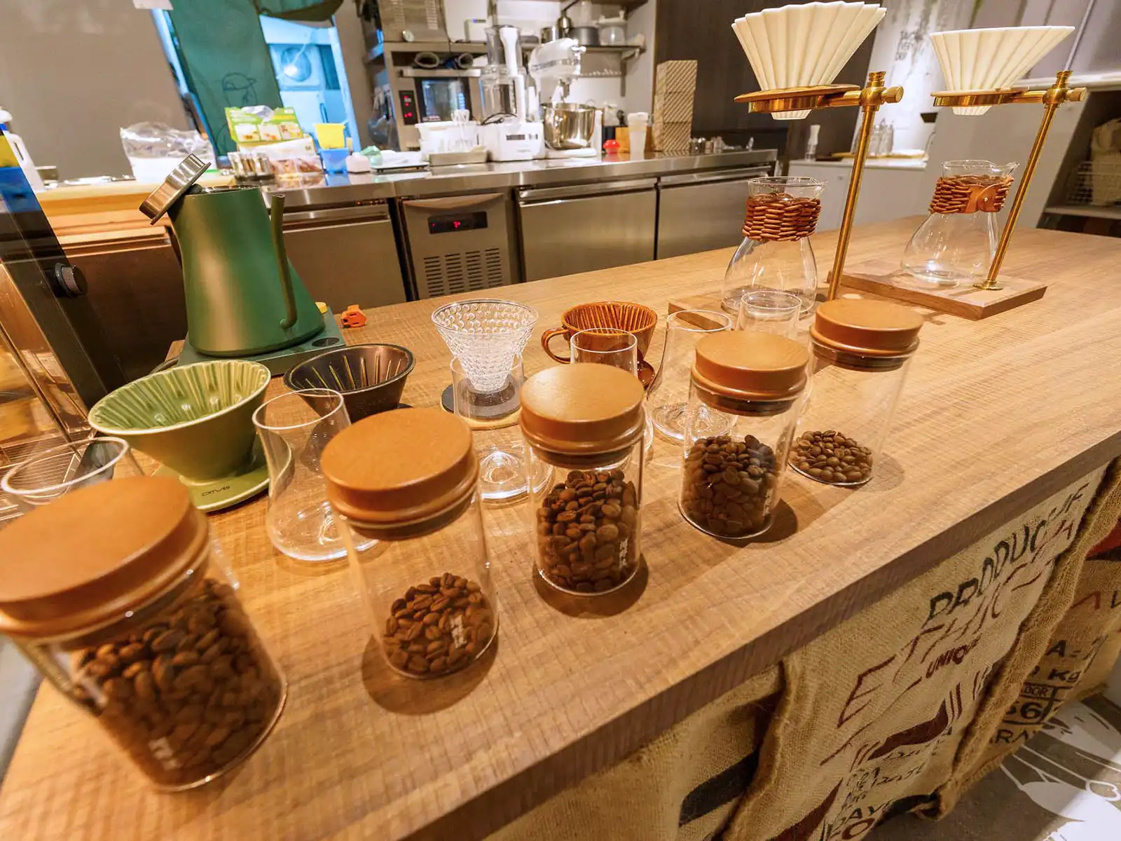 A selection of coffee beans displayed in jars with pour-over equipment on a wooden counter.