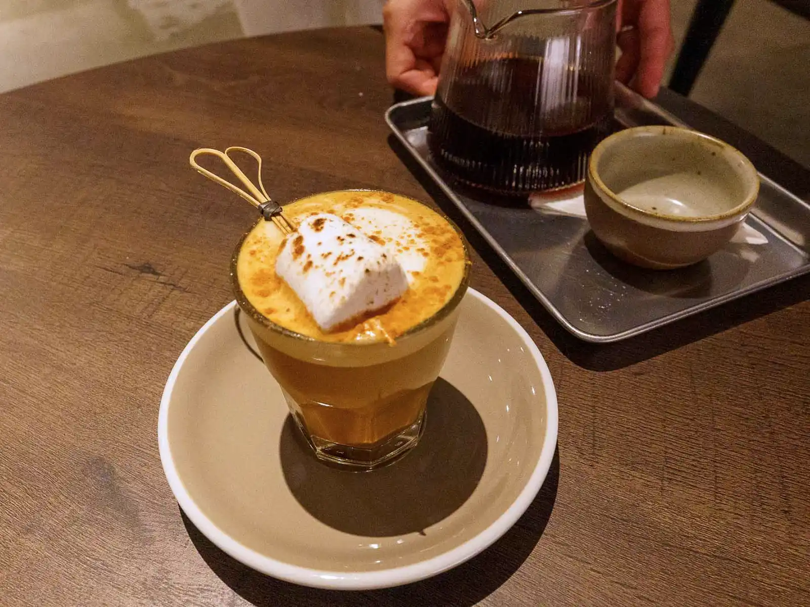 Aromatic coffee topped with a toasted marshmallow, served alongside a glass carafe.