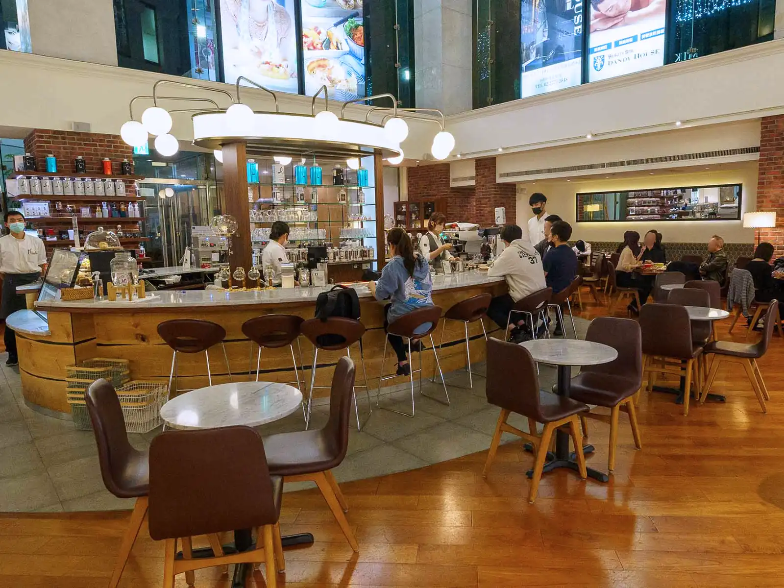 A bustling cafe interior with patrons seated at tables and baristas at work behind the counter.