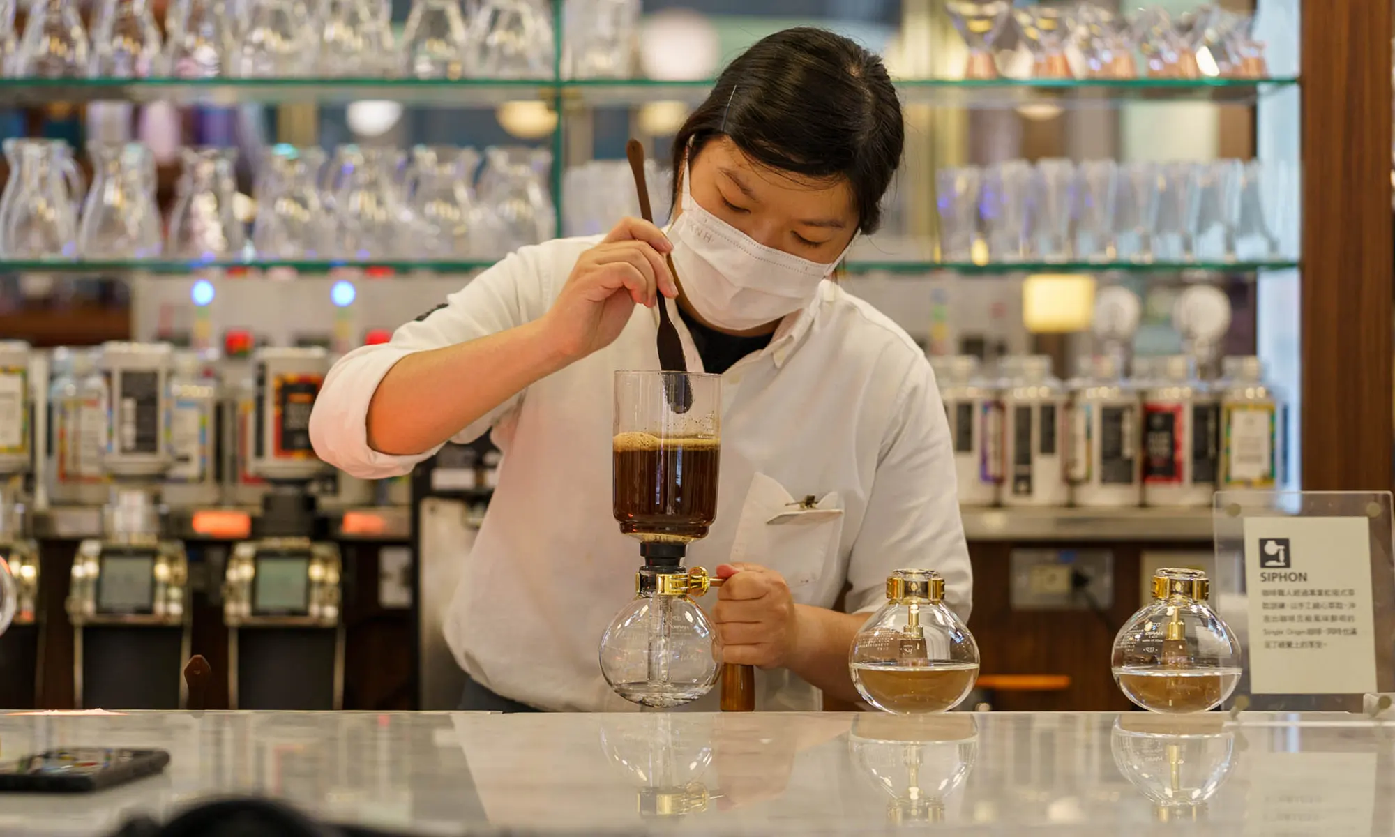 A barista attentively brews coffee using a siphon apparatus in a cafe.