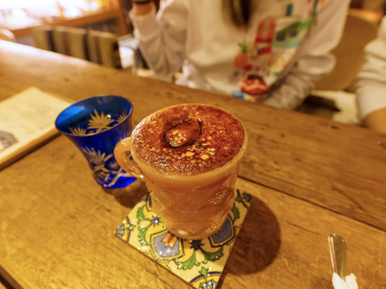 Gourmet caramel coffee topped with a cocoa dusted orange slice on a vibrant coaster.