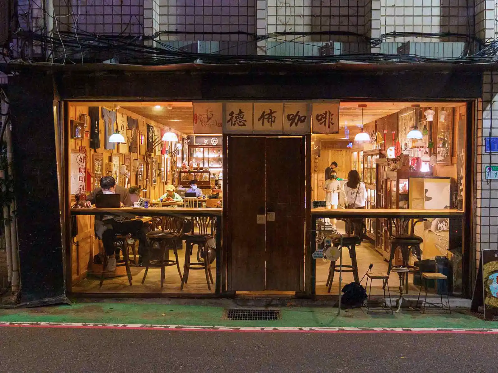 Exterior night view of a bustling Debut Cafe in Taipei with patrons inside.