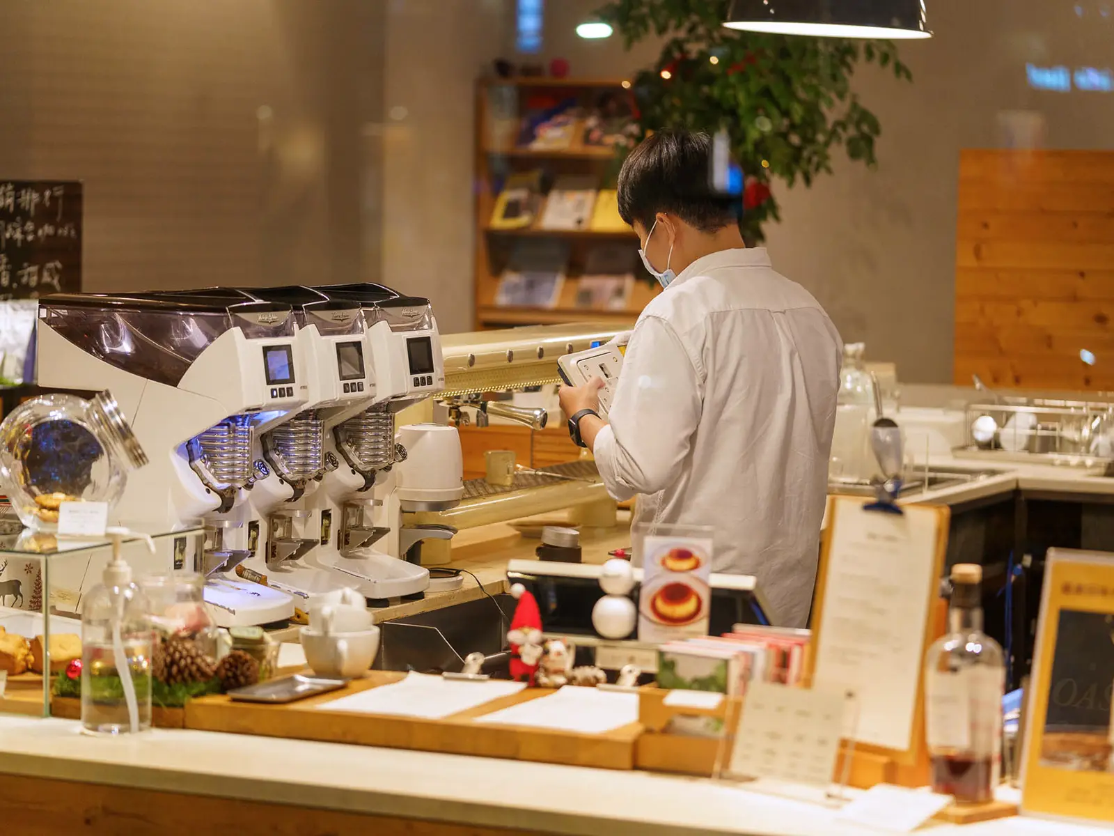 Barista at work behind a professional coffee machine in a warmly lit cafe.