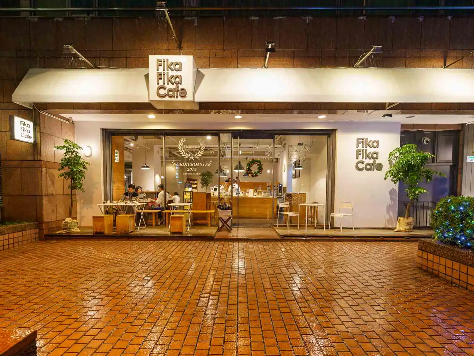 Exterior of Fika Fika Cafe in Taipei at night, warmly inviting with indoor seating visible.