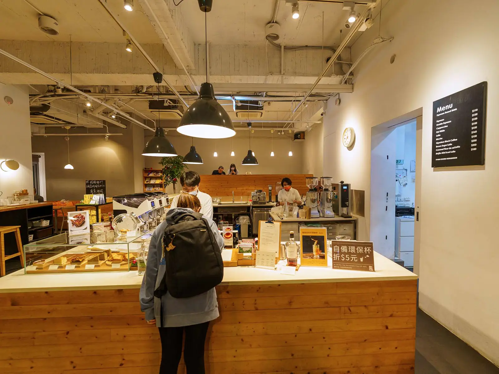 Customers at the counter of a modern, well-lit cafe with an array of coffee equipment.