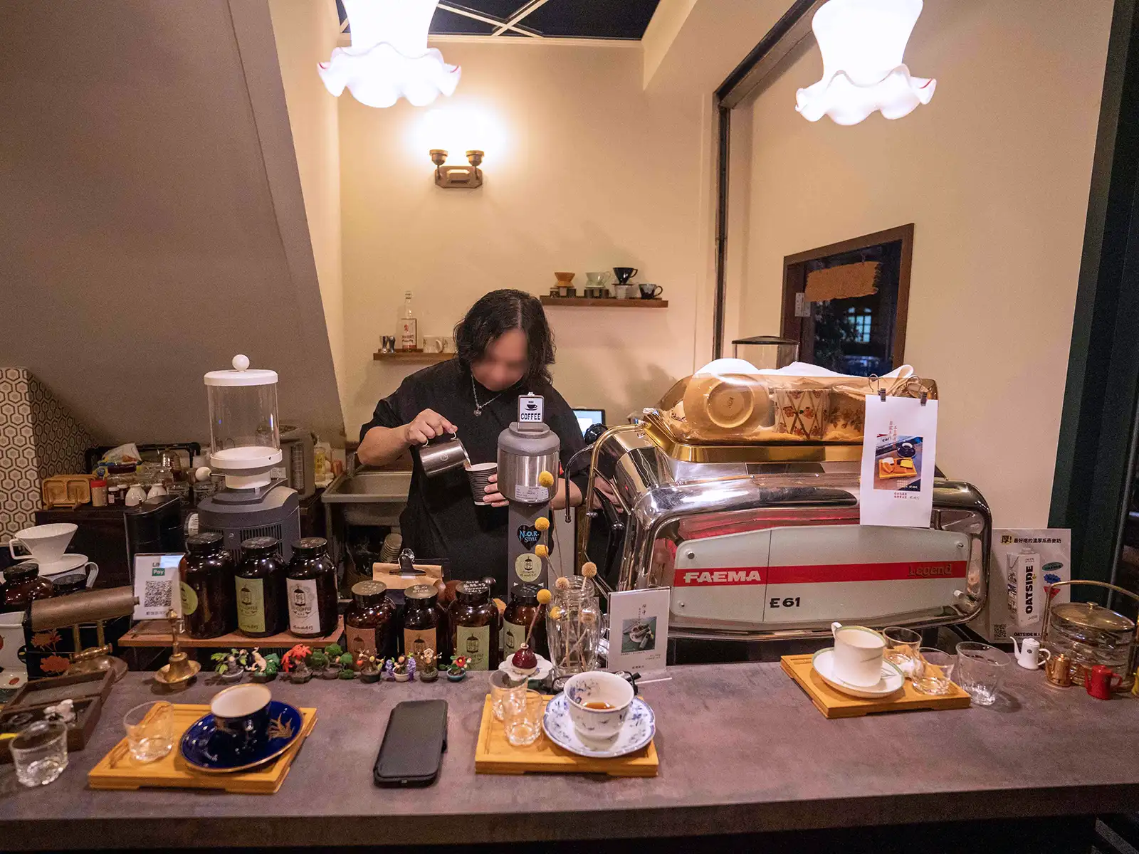 A focused barista pours steamed milk into a coffee cup in a warmly lit cafe.