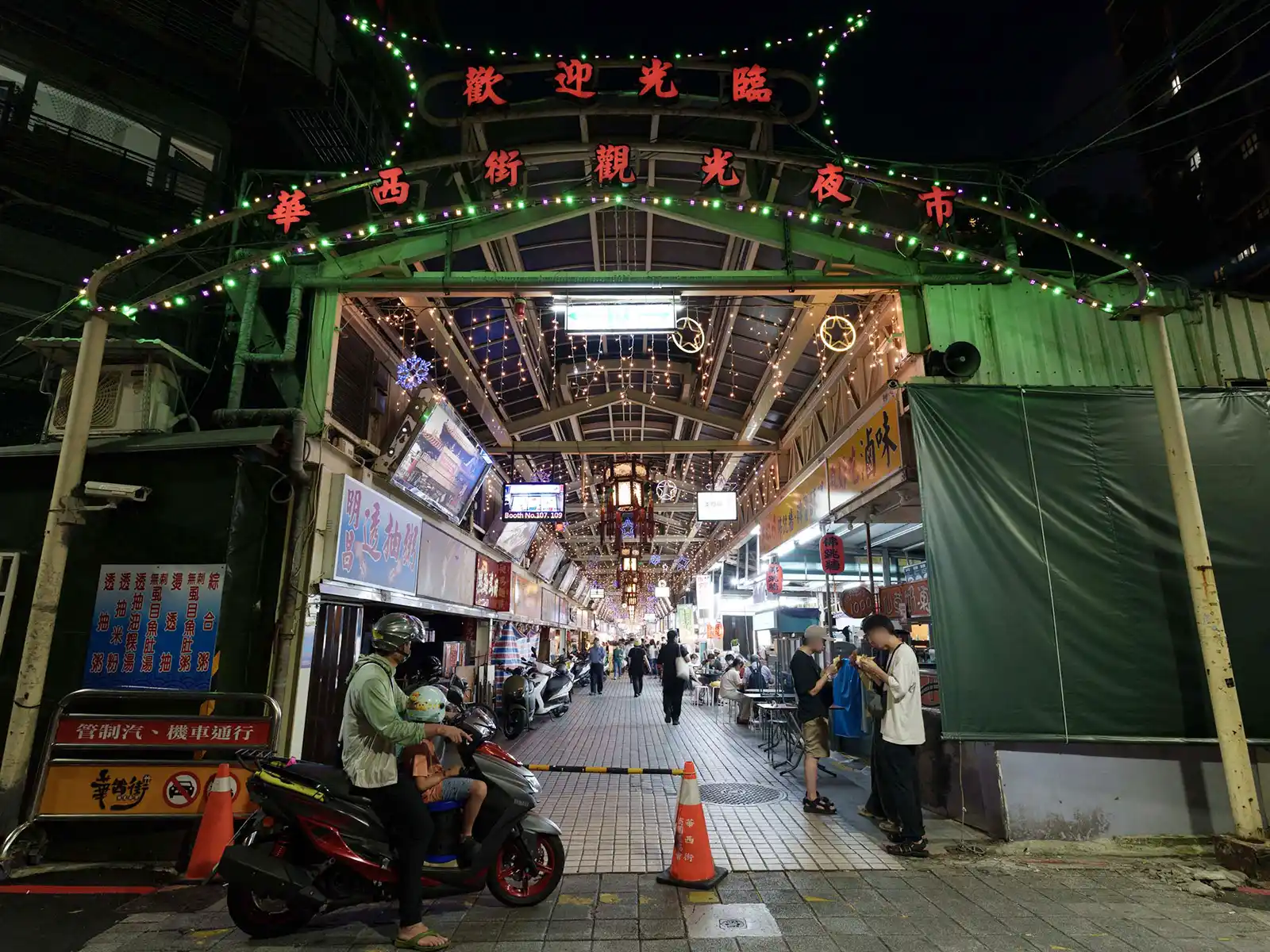 A bustling covered market street in Taipei illuminated with green decorative lights at night.