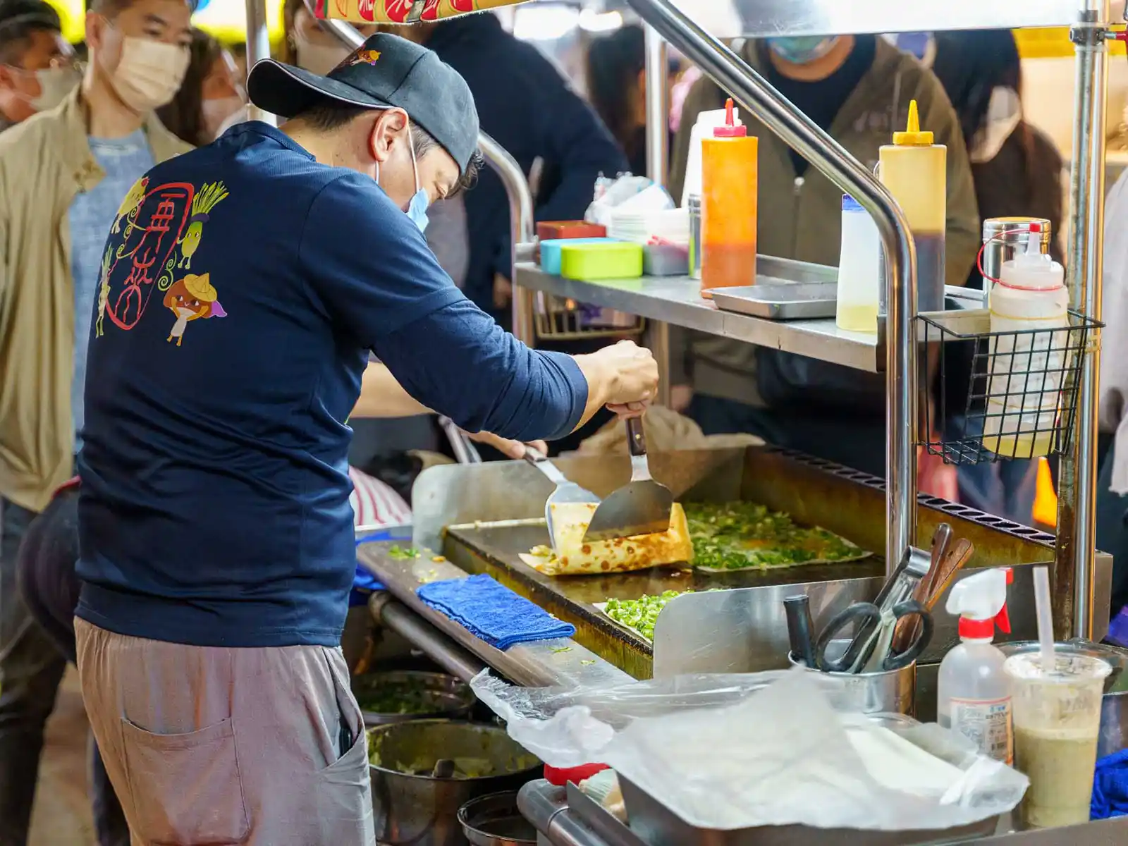 A vendor prepares fried dough with scallions at a bustling night market stall.