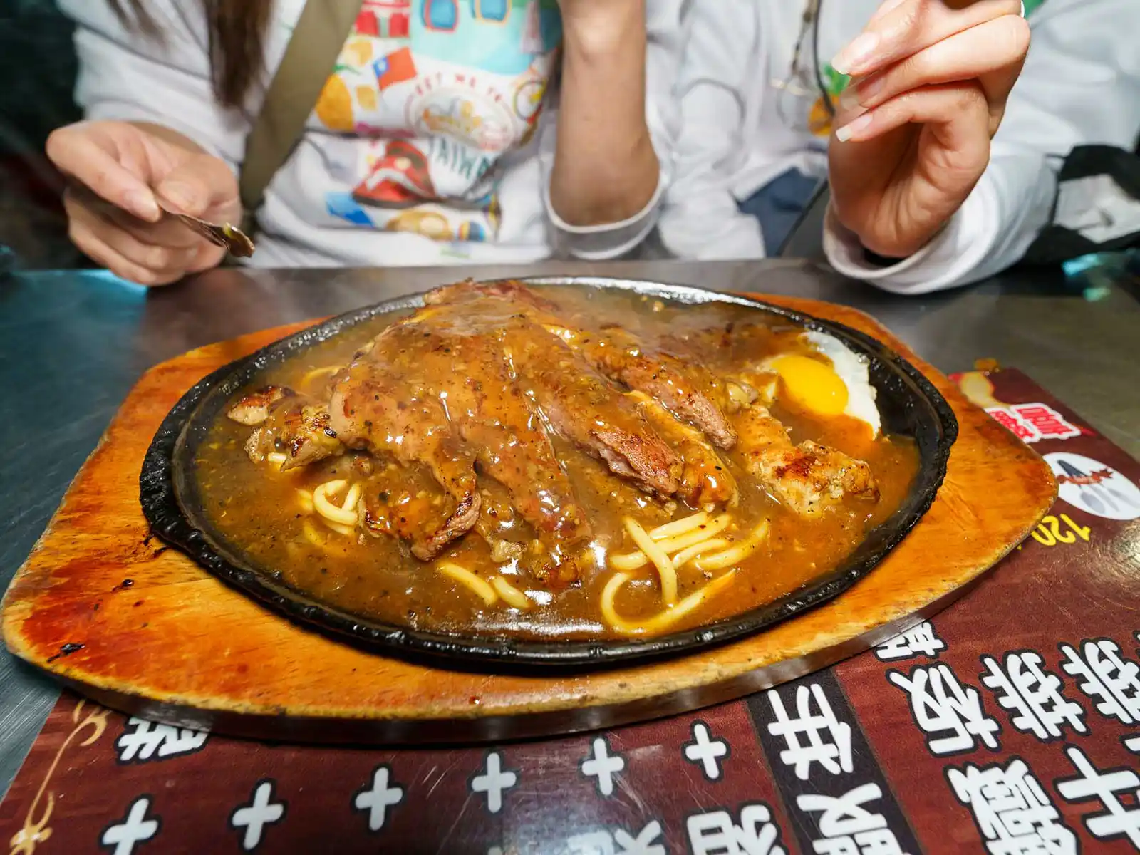 A close-up of a sizzling steak and egg dish on a hot plate.